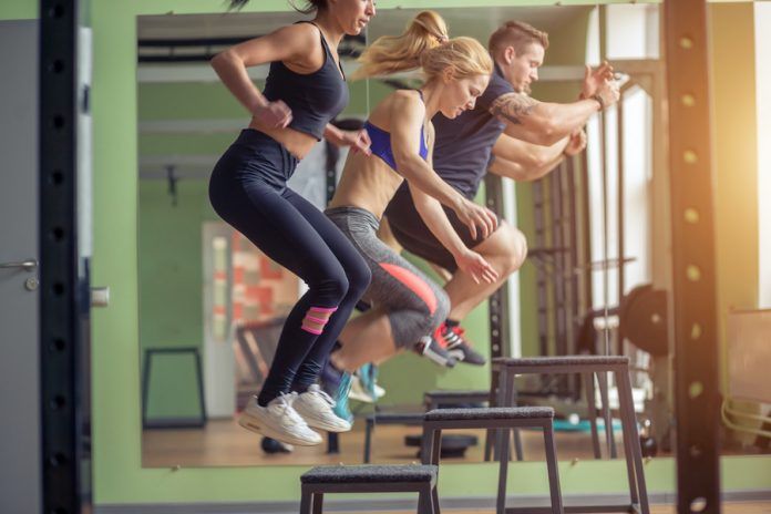 Male And Female Athletes Doing Box Jumps At Gym