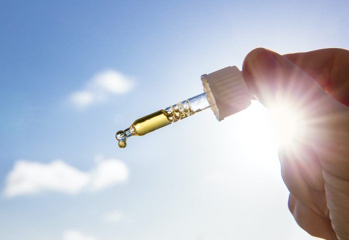 Hand Holding Dropper Pipette With Nice Golden Liquid D Vitamin Against Sun And Blue Sky On Sunny Day. Vitamin D Keeps You Healthy While Lack Of Sun In Winter, Cure Concept.