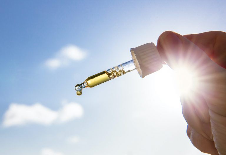 Hand Holding Dropper Pipette With Nice Golden Liquid D Vitamin Against Sun And Blue Sky On Sunny Day. Vitamin D Keeps You Healthy While Lack Of Sun In Winter, Cure Concept.